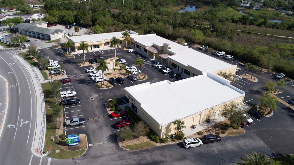 An aerial view shows a commercial plaza with multiple buildings, parking lots, and palm trees — 24420 SANDHILL BOULEVARD, PUNTA GORDA, FL
