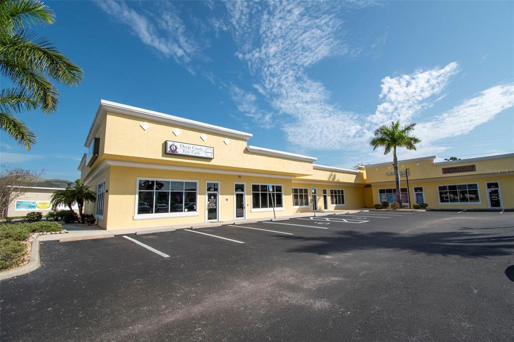 A yellow commercial strip mall building with a parking lot under a blue sky — 24420 SANDHILL BOULEVARD, PUNTA GORDA, FL