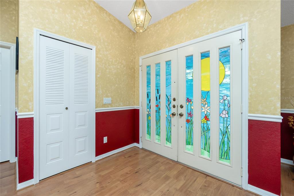An entryway features wood flooring, red and yellow walls, a louvered closet, and stained-glass double doors — 4088 GINGOLD STREET, PORT CHARLOTTE, FL