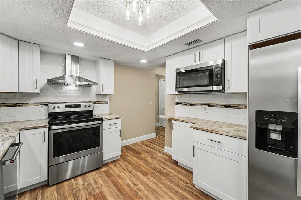 A kitchen with white cabinets, stainless steel appliances, granite countertops, and wood-look flooring — 1364 DILL AVENUE, SPRING HILL, FL