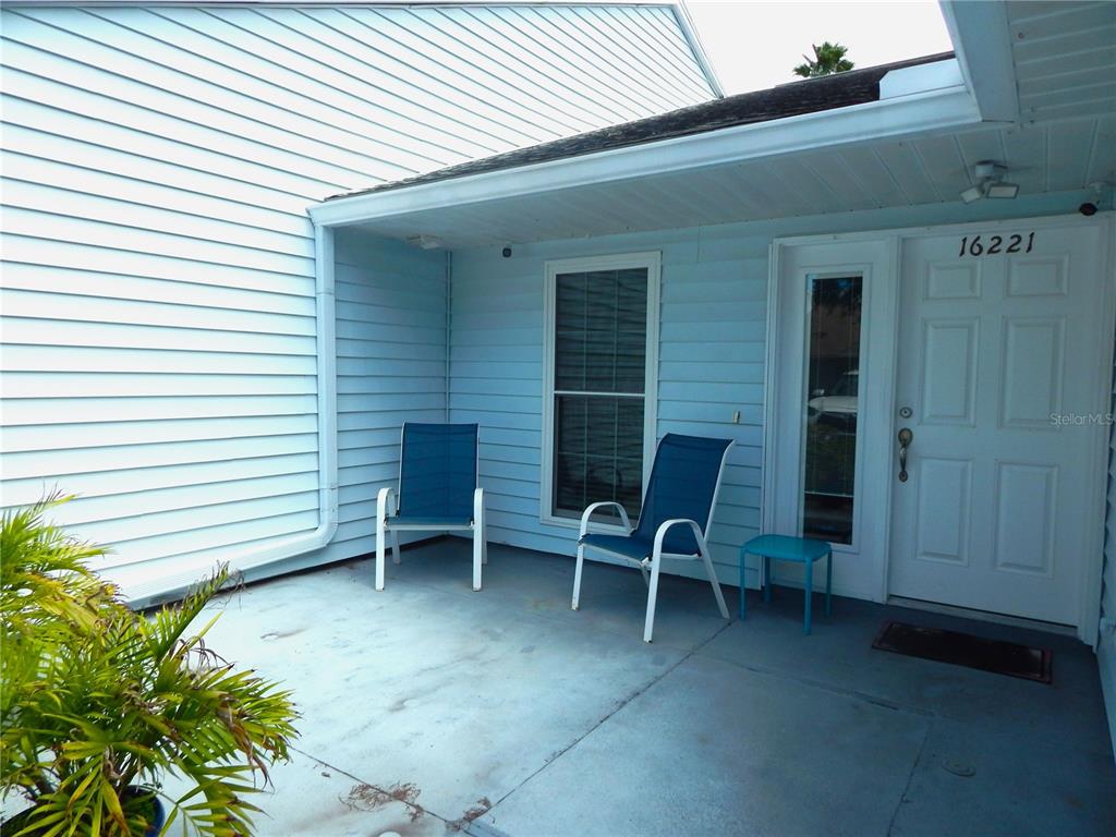 A light blue house exterior features a covered porch with two chairs and a door — 16221 RAMBLING VINE DRIVE W, TAMPA, FL