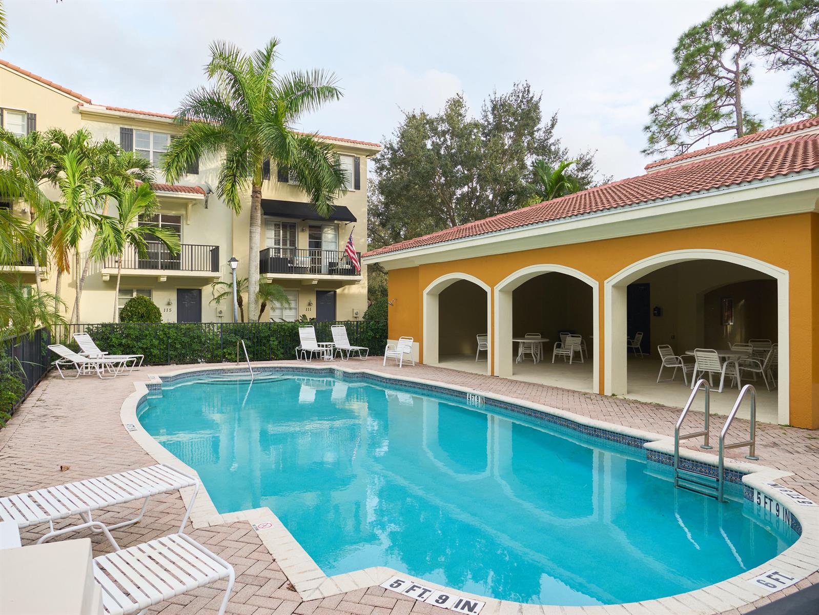 A swimming pool with a brick deck sits beside a multi-story building and covered patio — 405 Schoolhouse Road, Jupiter FL 33458, JUPITER, FL