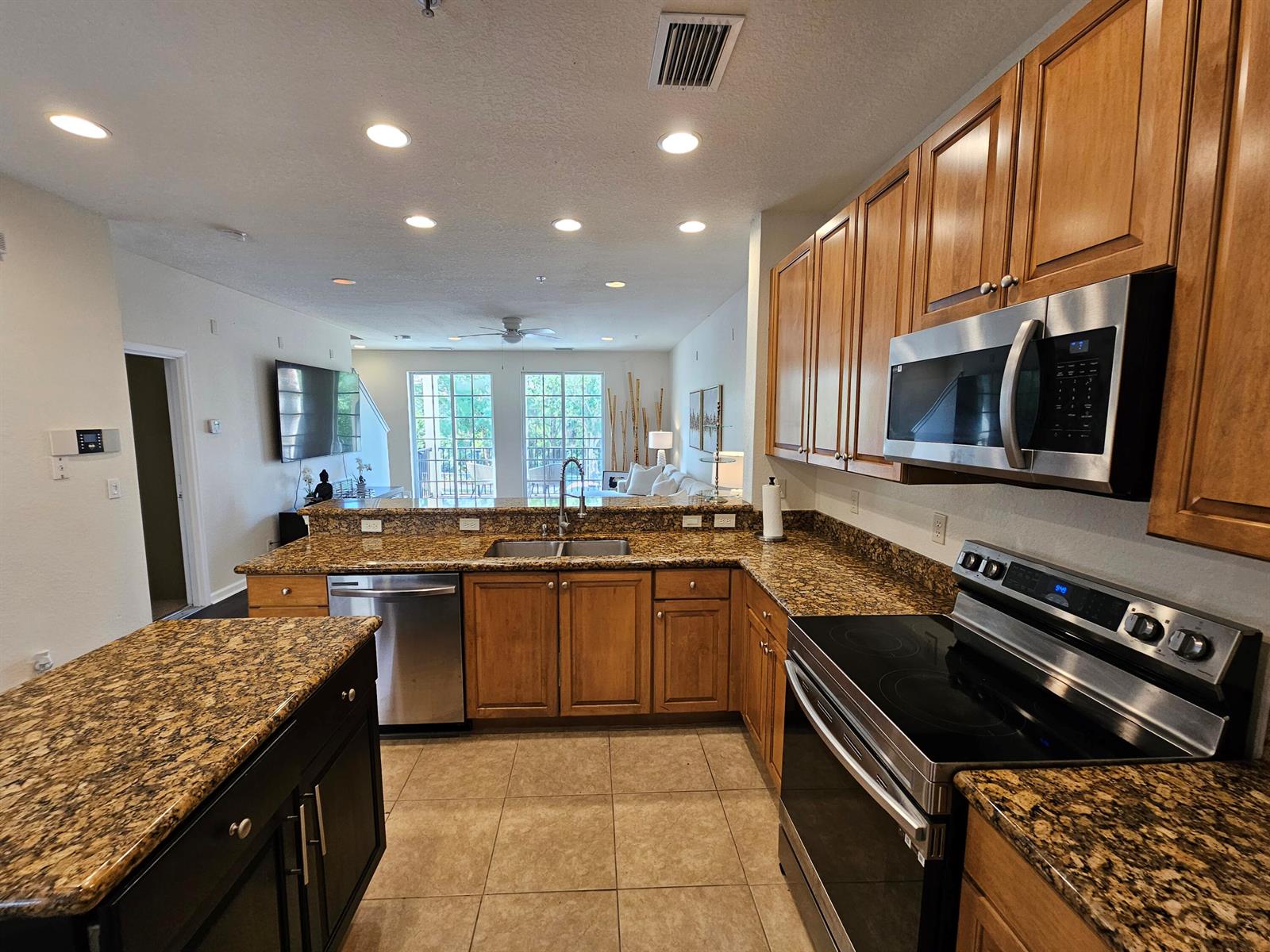 A kitchen with granite countertops, wood cabinets, and stainless steel appliances overlooks an open living area — 405 Schoolhouse Road, Jupiter FL 33458, JUPITER, FL