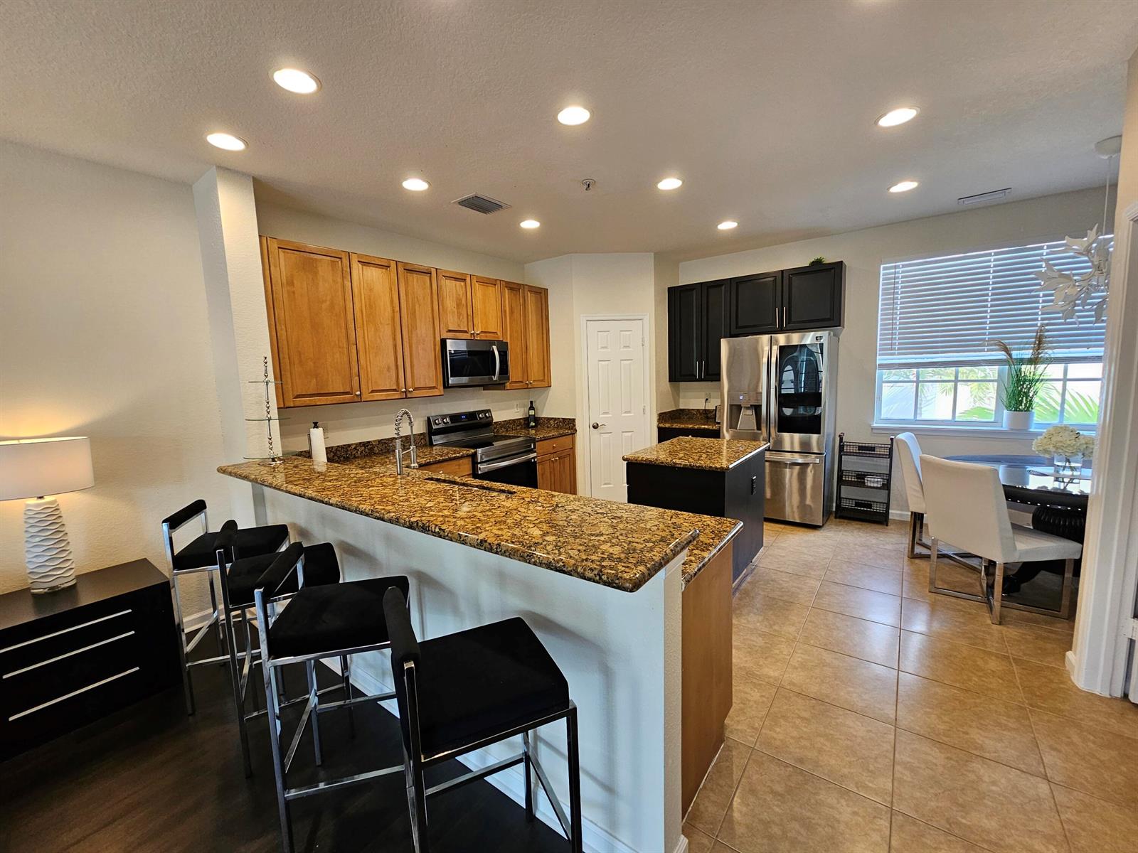 A kitchen features wood and black cabinetry, granite countertops, a breakfast bar, and tile flooring — 405 Schoolhouse Road, Jupiter FL 33458, JUPITER, FL