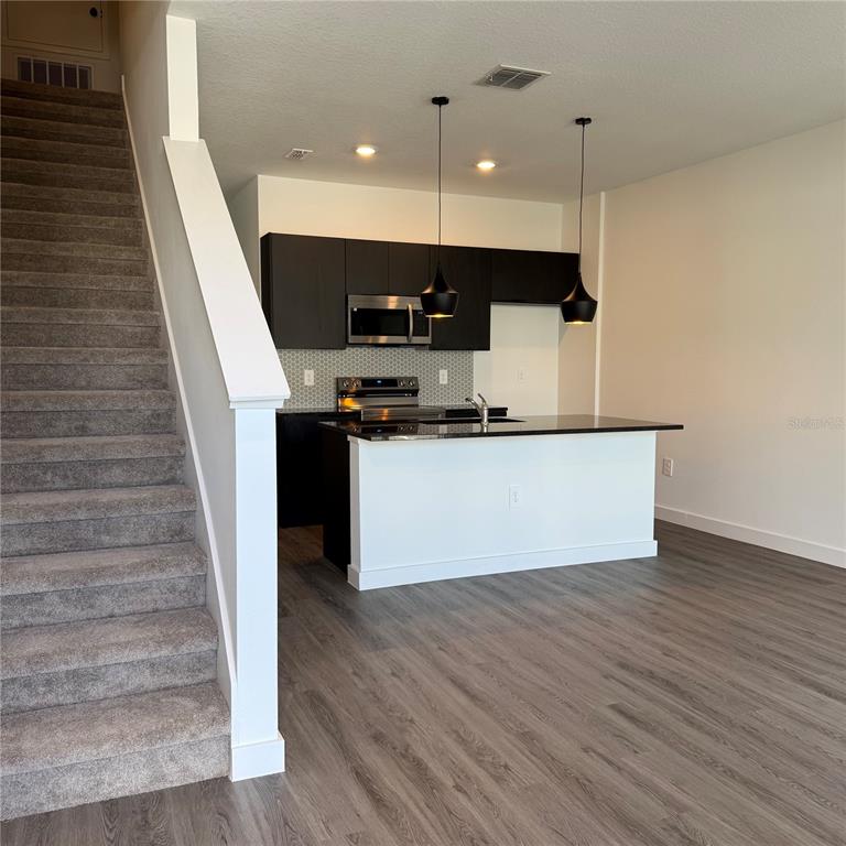 A kitchen with dark cabinets and a breakfast bar sits beside a carpeted staircase — 3245 SUSTAINABLE WAY, KISSIMMEE, FL
