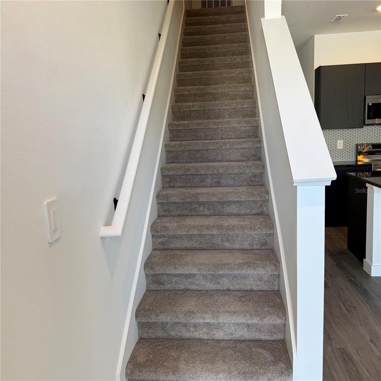 A carpeted staircase with a white handrail leads upward between two interior walls — 3245 SUSTAINABLE WAY, KISSIMMEE, FL