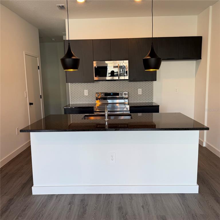 A modern kitchen features a white island, dark cabinetry, stainless steel appliances, and pendant lighting — 3245 SUSTAINABLE WAY, KISSIMMEE, FL