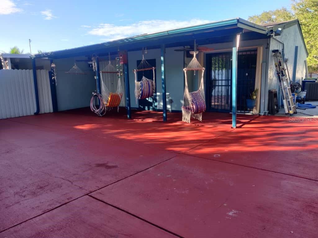 A covered patio with a red concrete floor features three hanging chairs under a roof — 21348 NW 40TH CIRCLE COURT, MIAMI GARDENS, FL