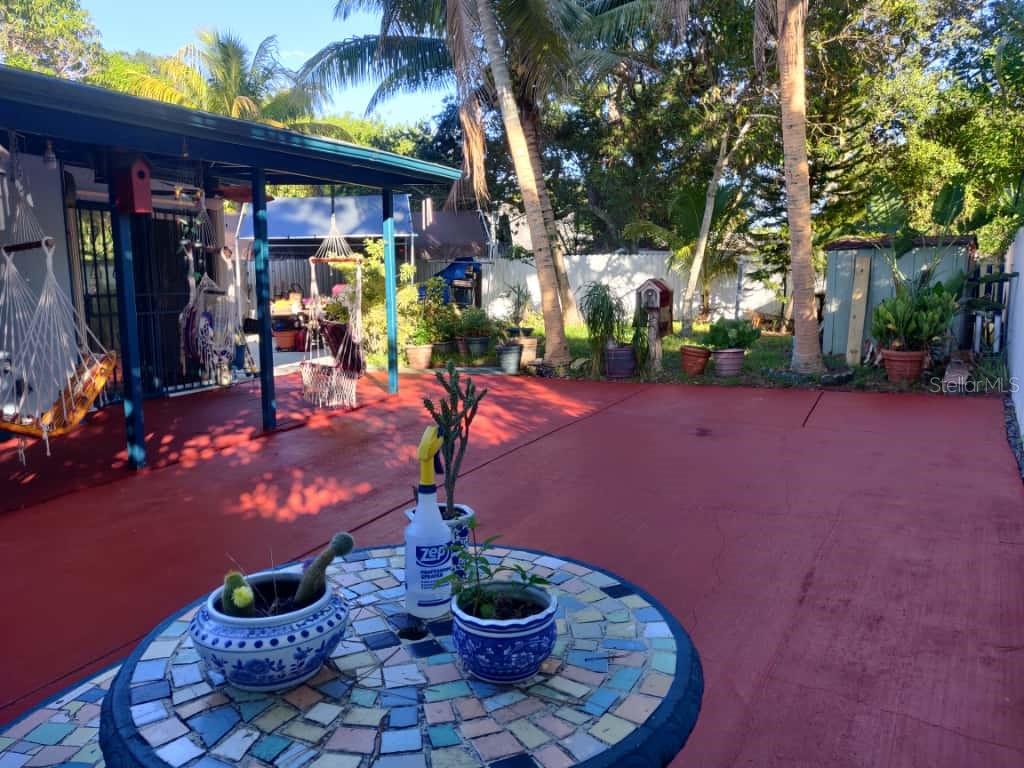 A red-painted patio features a mosaic-tiled table, potted plants, and hanging chairs under a roof — 21348 NW 40TH CIRCLE COURT, MIAMI GARDENS, FL