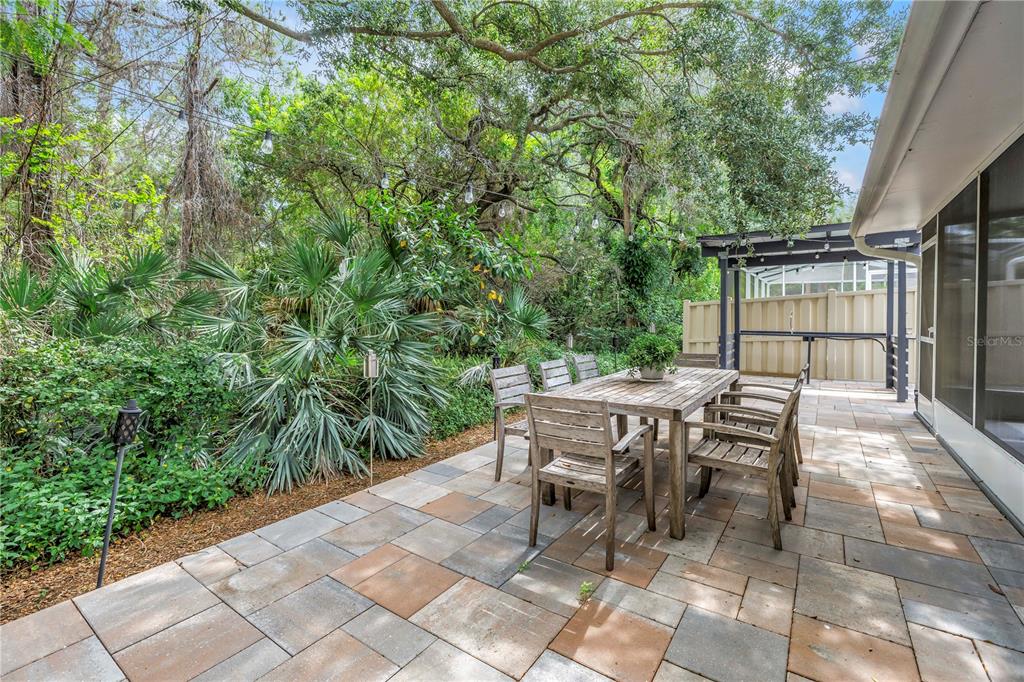 A patio with a wooden dining set sits beside a house under large trees — 355 RED CEDAR COURT NE, ST PETERSBURG, FL