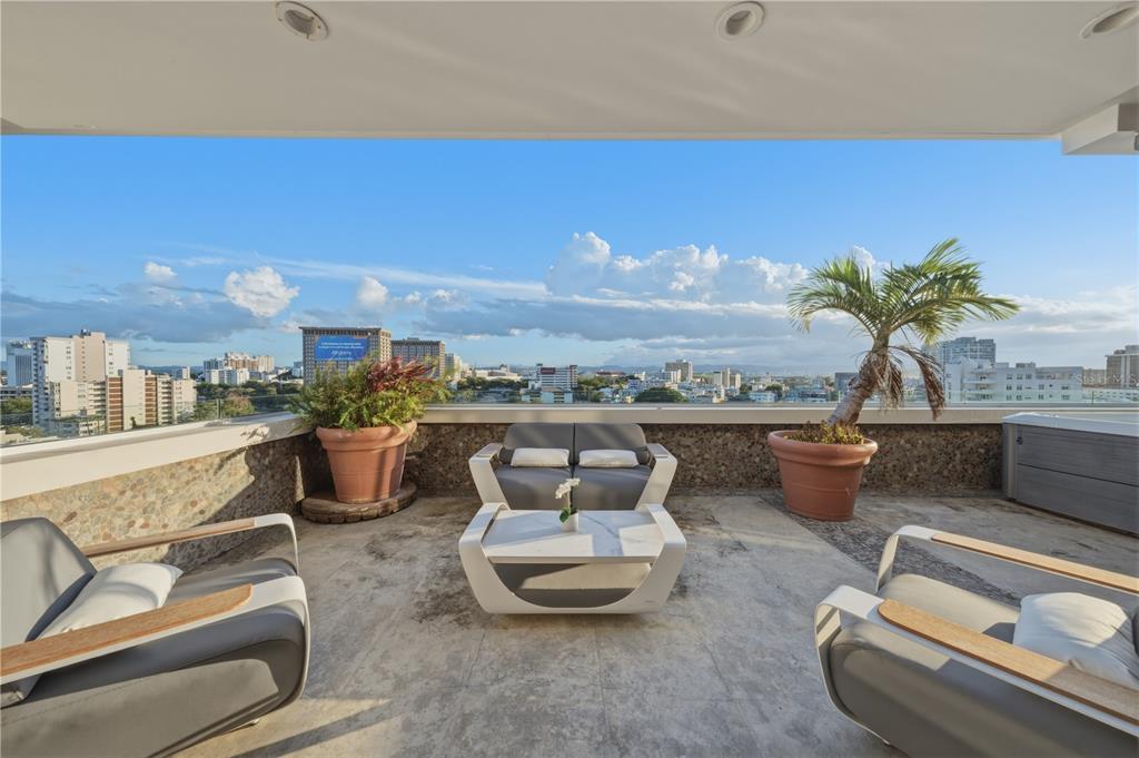 A rooftop terrace features modern outdoor furniture, potted plants, and a panoramic city skyline view — 1354 LUCHETTI STREET UNIT PH, SAN JUAN, PR