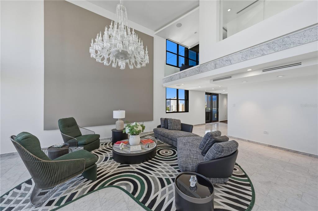 A modern living room features a large crystal chandelier, high ceilings, and a patterned rug — 1354 LUCHETTI STREET UNIT PH, SAN JUAN, PR