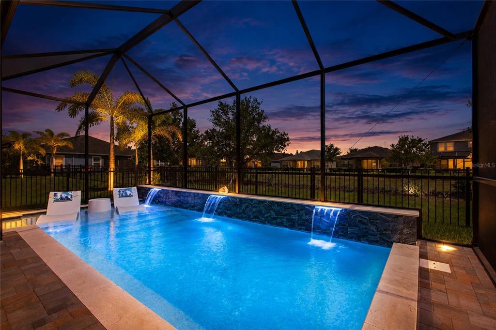 A swimming pool with two water features sits inside a screened lanai at dusk — 6109 COLMAR PLACE, APOLLO BEACH, FL