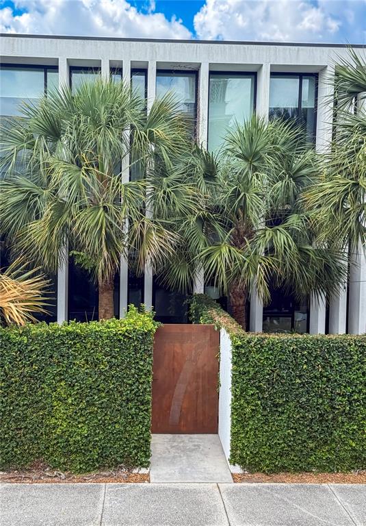 A modern building exterior features a rusted metal gate flanked by tall hedges and palms — 154 2ND STREET SW Unit 7, WINTER HAVEN, FL