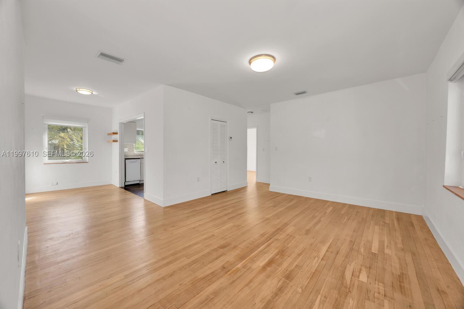An empty room features light hardwood floors, white walls, and a doorway to a kitchen — 5510 SW 76th St # C, Miami FL 33143, MIAMI, FL