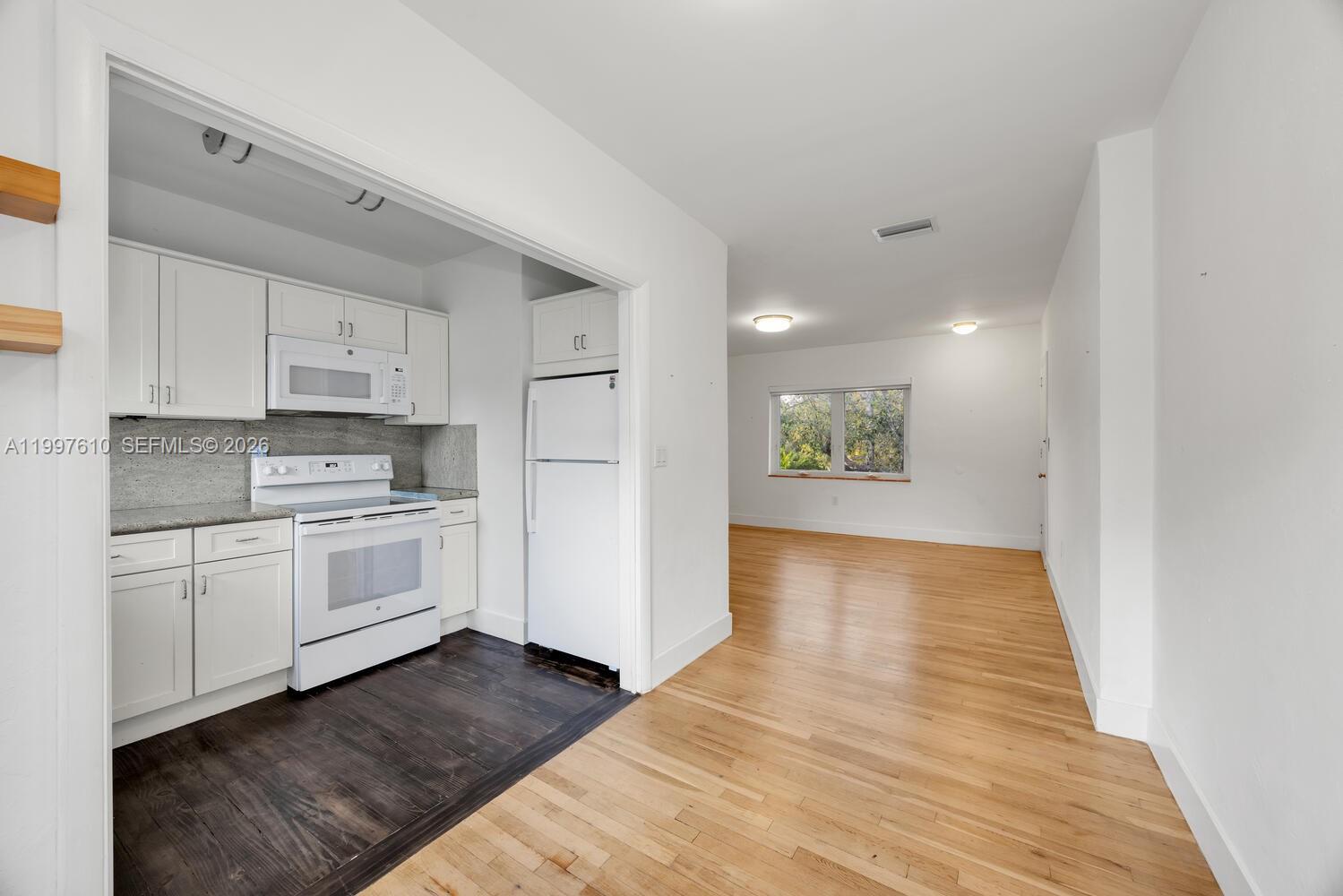 A kitchen with white cabinets and dark flooring opens into a living area with hardwood floors — 5510 SW 76th St # C, Miami FL 33143, MIAMI, FL
