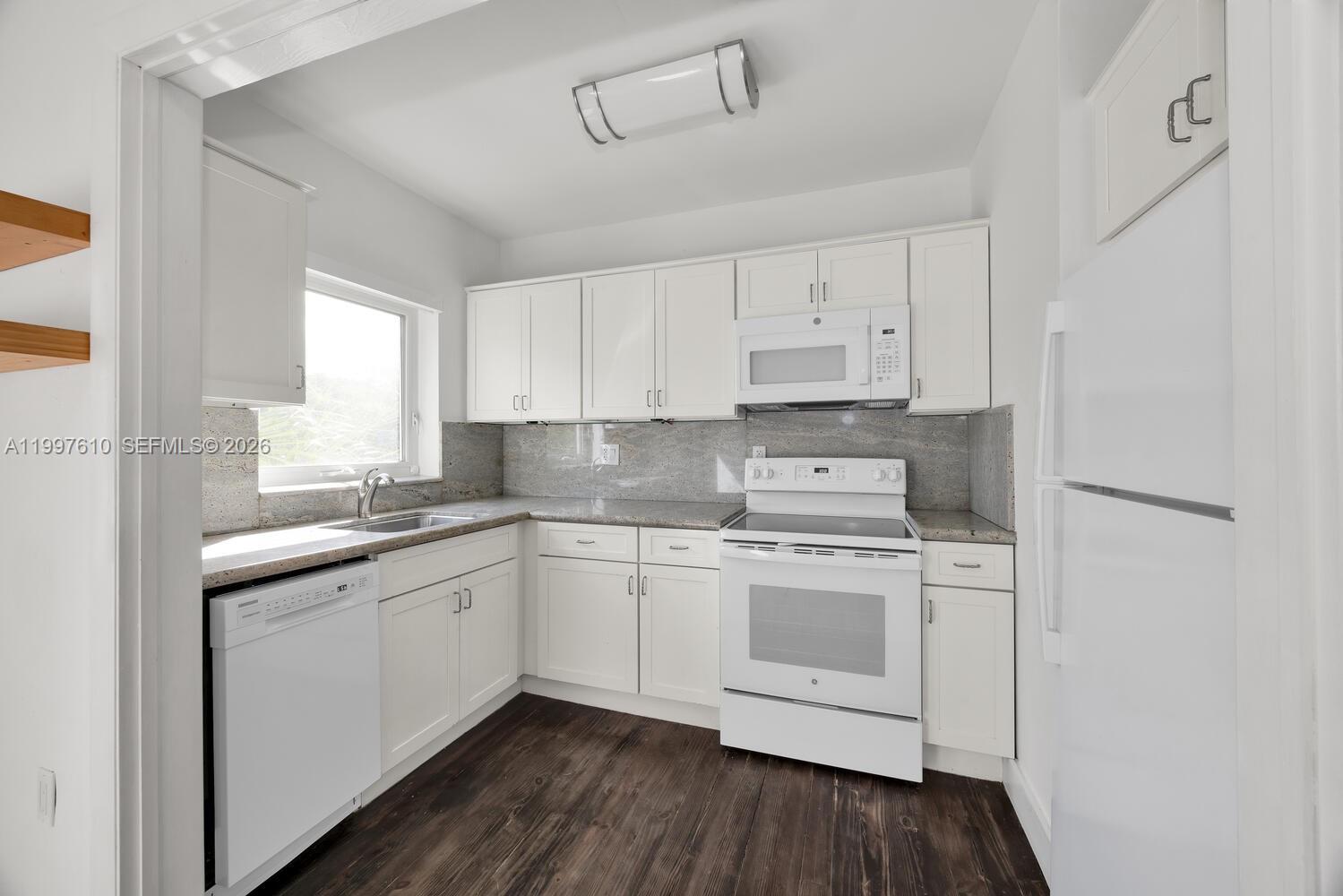 A white kitchen features dark wood flooring, granite countertops, and stainless steel appliances — 5510 SW 76th St # C, Miami FL 33143, MIAMI, FL