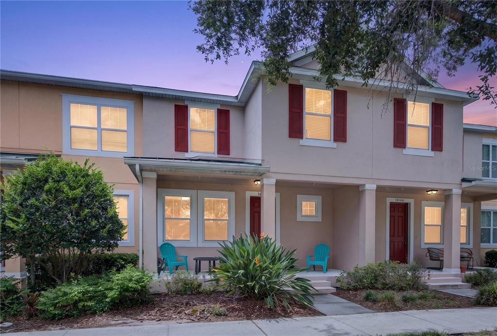 A two-story townhouse exterior features beige stucco walls, red shutters, and a covered front porch — 10148 HARTFORD MAROON ROAD, ORLANDO, FL