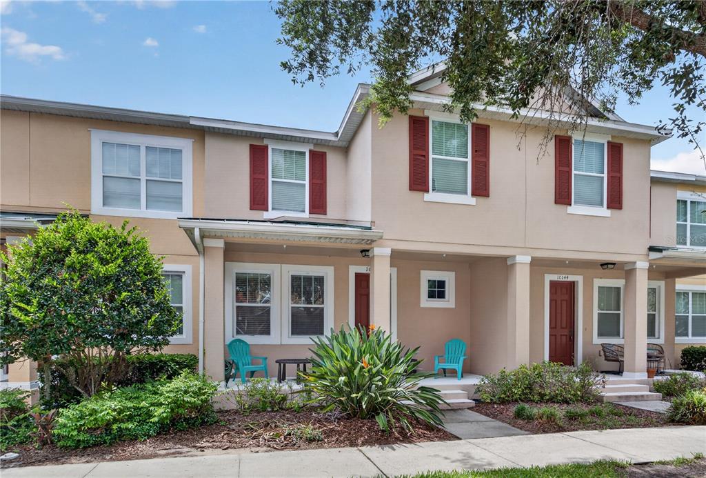 A two-story townhouse exterior with beige stucco walls, red shutters, and a covered front porch — 10148 HARTFORD MAROON ROAD, ORLANDO, FL