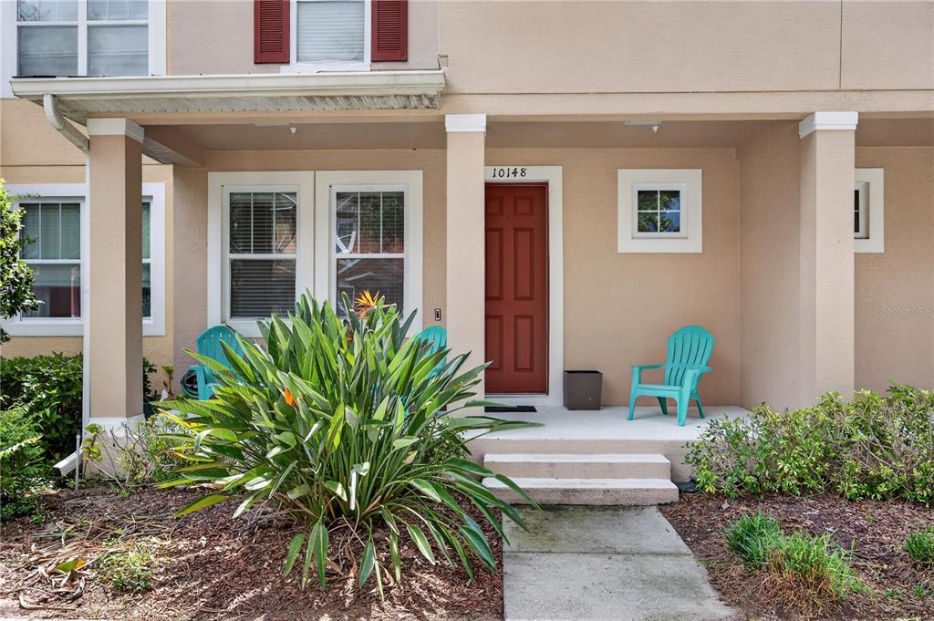 A tan house exterior features a red front door, a covered porch, and turquoise chairs — 10148 HARTFORD MAROON ROAD, ORLANDO, FL