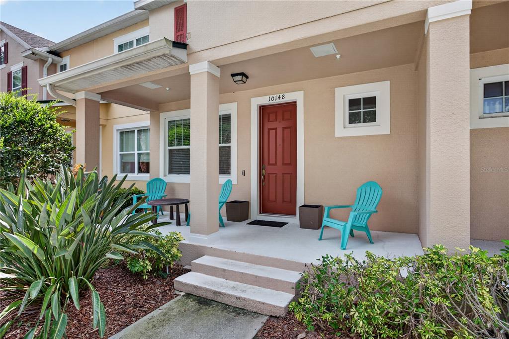 A tan house exterior features a covered front porch with a red door and chairs — 10148 HARTFORD MAROON ROAD, ORLANDO, FL