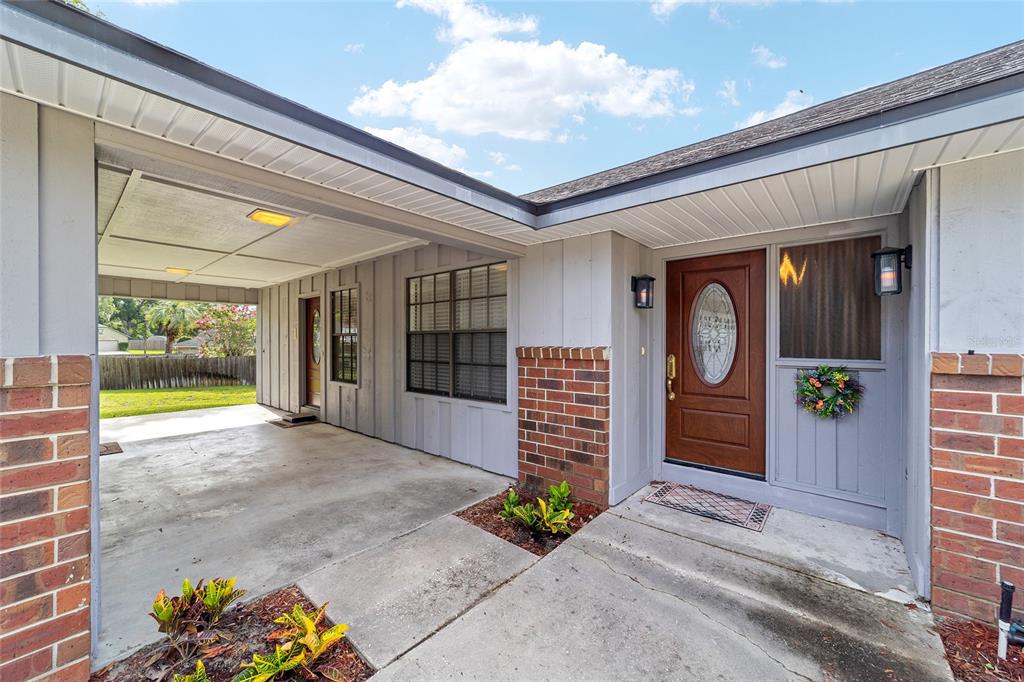 A gray house exterior features a concrete carport, brick accents, and a wooden front door — 4508 SE 2ND PLACE, OCALA, FL