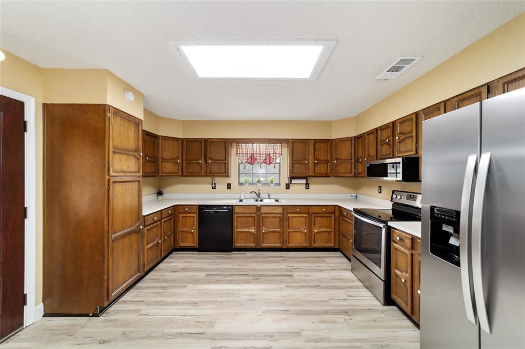 A kitchen features wood cabinets, stainless steel appliances, a black dishwasher, and light wood flooring — 4508 SE 2ND PLACE, OCALA, FL