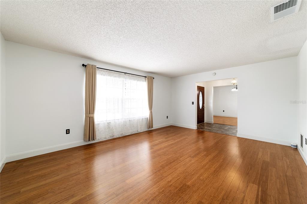 An empty living room with white walls, wood flooring, and a large window with curtains — 4508 SE 2ND PLACE, OCALA, FL