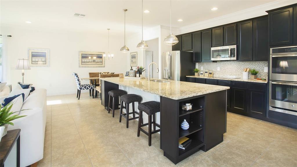 A kitchen with dark cabinets, a granite island, and bar stools opens to a dining area — 25147 CALUSA DRIVE, PUNTA GORDA, FL