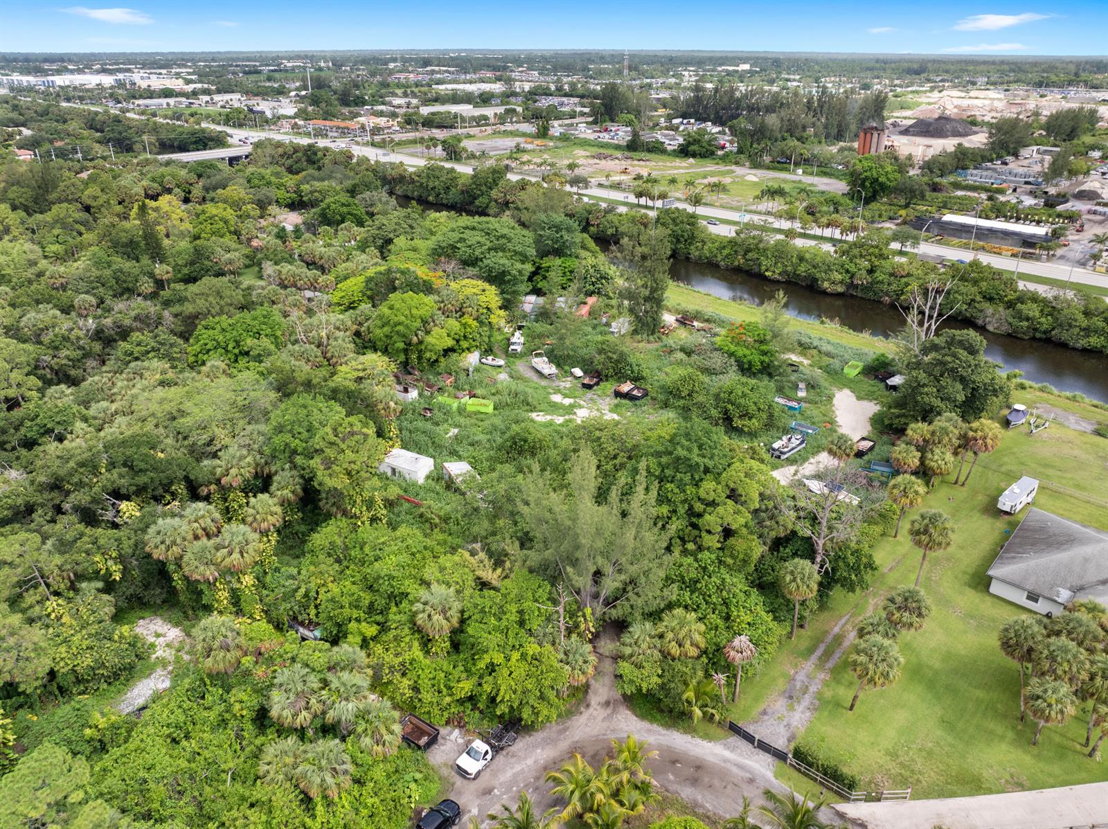 An aerial view shows a wooded lot with scattered debris, vehicles, and a nearby canal — 69 Armadillo Way, West Palm Beach FL 33411, WEST PALM BEACH, FL
