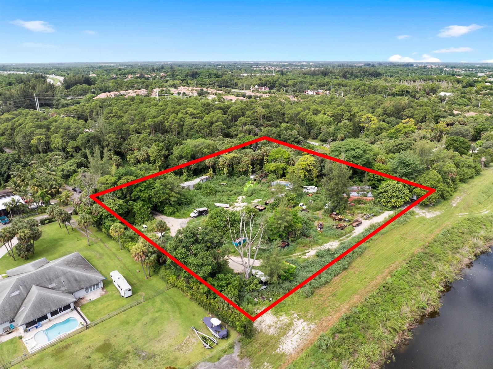 An aerial view shows a large, overgrown, rectangular lot outlined in red next to a canal — 69 Armadillo Way, West Palm Beach FL 33411, WEST PALM BEACH, FL