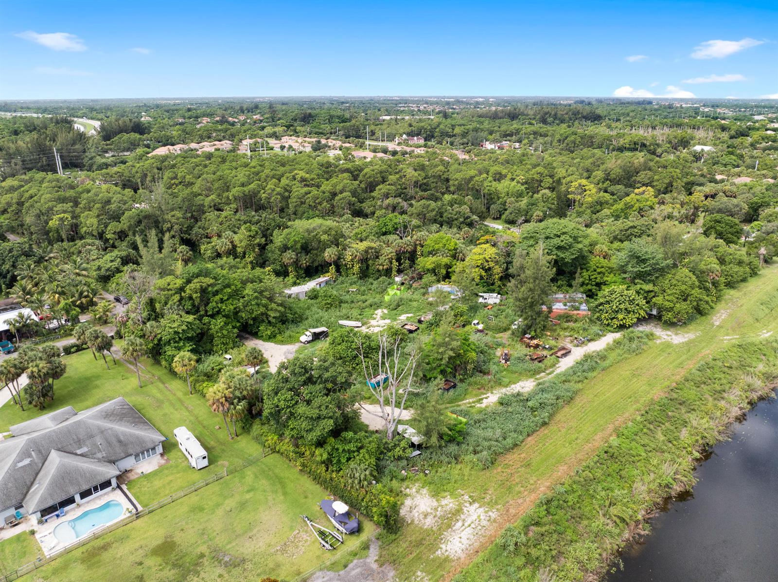 An aerial view shows a house with a pool next to a large, wooded lot — 69 Armadillo Way, West Palm Beach FL 33411, WEST PALM BEACH, FL