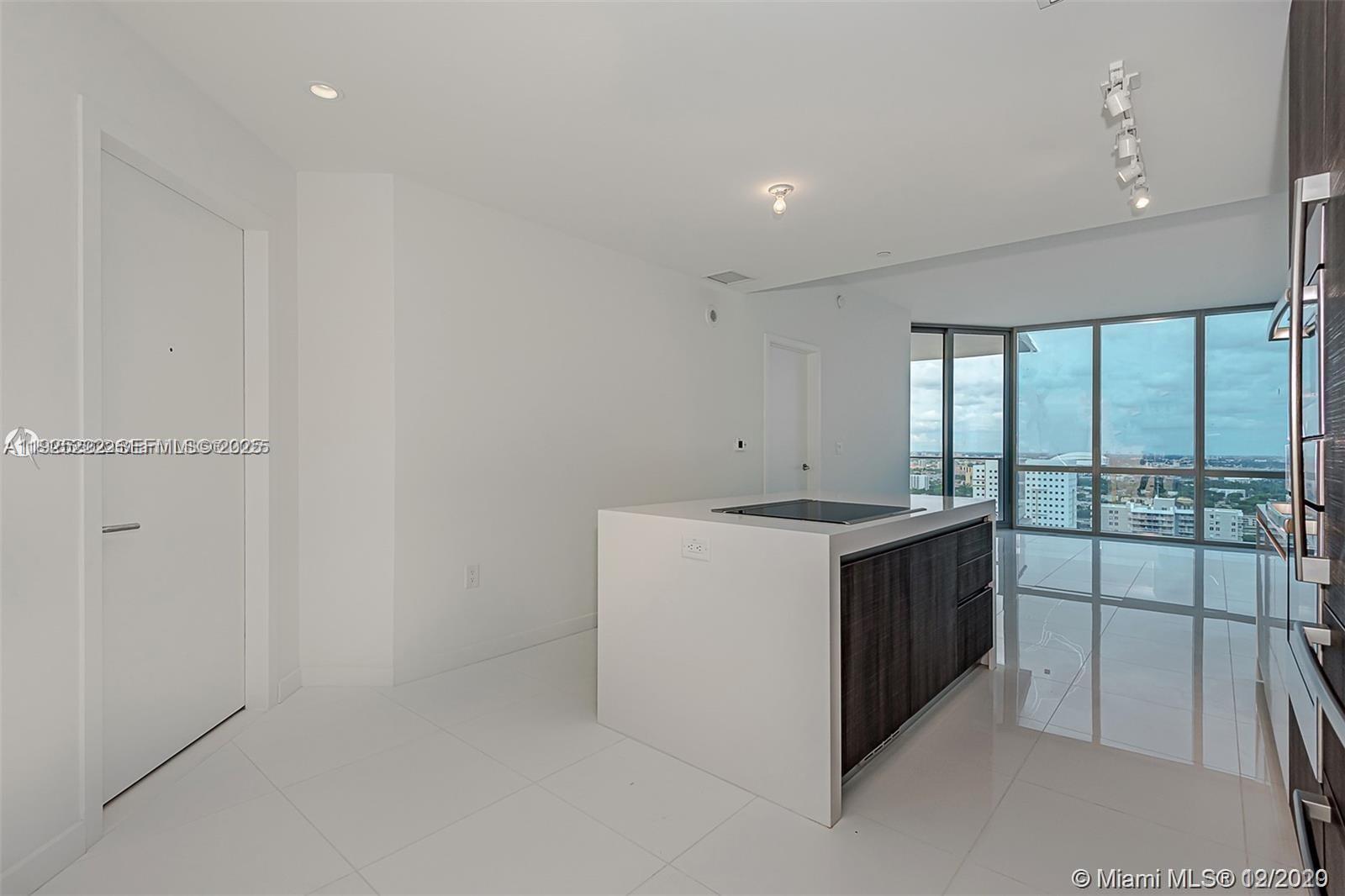 A modern kitchen features a central island with a dark wood cabinet and white countertop — 851 NE 1st Ave # 1608, Miami FL 33132, MIAMI, FL