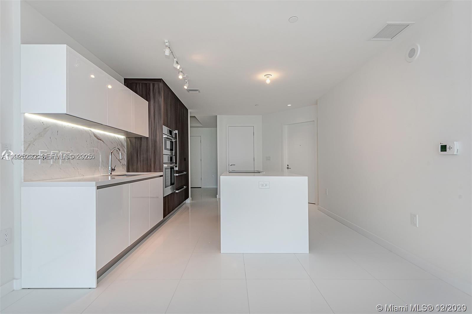 A modern kitchen features white cabinetry, a marble backsplash, and a central island — 851 NE 1st Ave # 1608, Miami FL 33132, MIAMI, FL