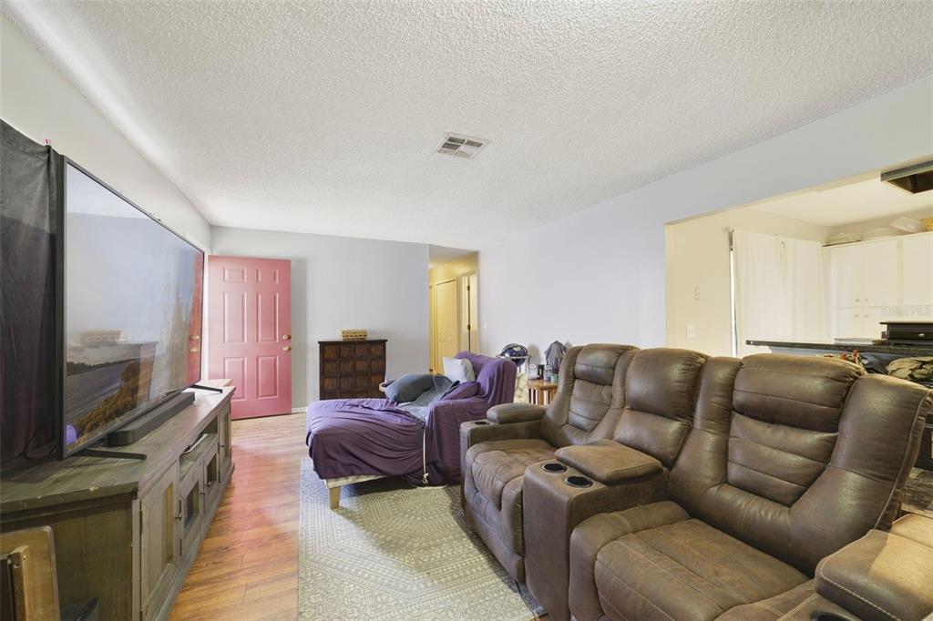 A living room features a large television, brown reclining sofa, purple chaise, and pink door — 5909 TURNBULL DRIVE, ORLANDO, FL