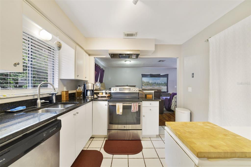 A kitchen with white cabinets, stainless steel appliances, and a pass-through to the living room — 5909 TURNBULL DRIVE, ORLANDO, FL
