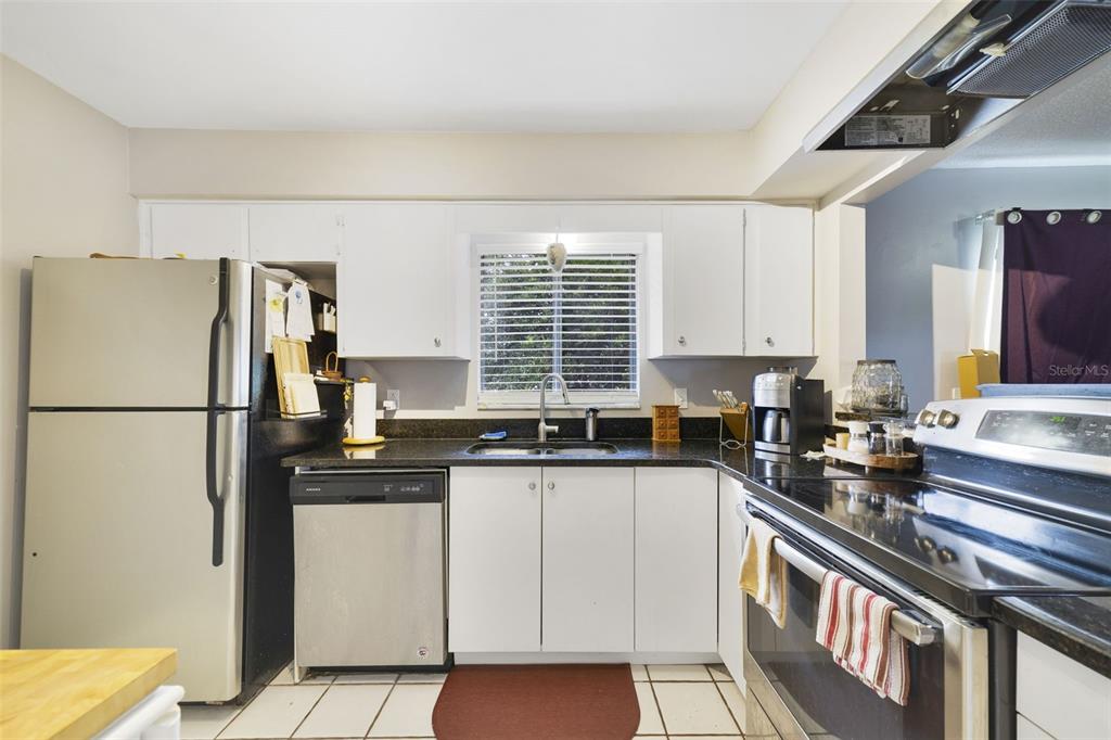 A kitchen features white cabinets, black countertops, stainless steel appliances, and white tile flooring — 5909 TURNBULL DRIVE, ORLANDO, FL