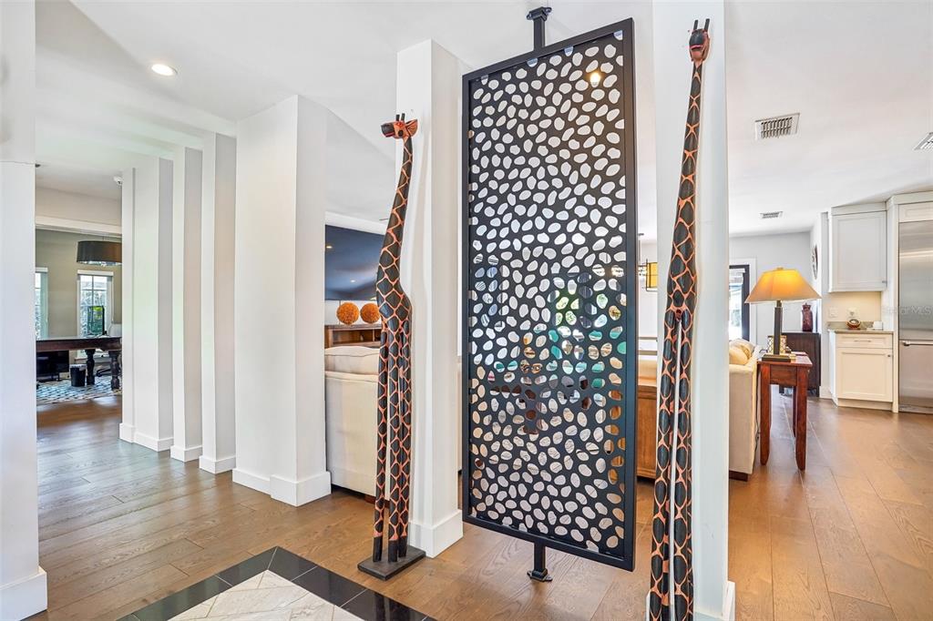 A decorative black metal screen stands between two wooden giraffe statues in a bright hallway — 1271 PALMER AVENUE, WINTER PARK, FL