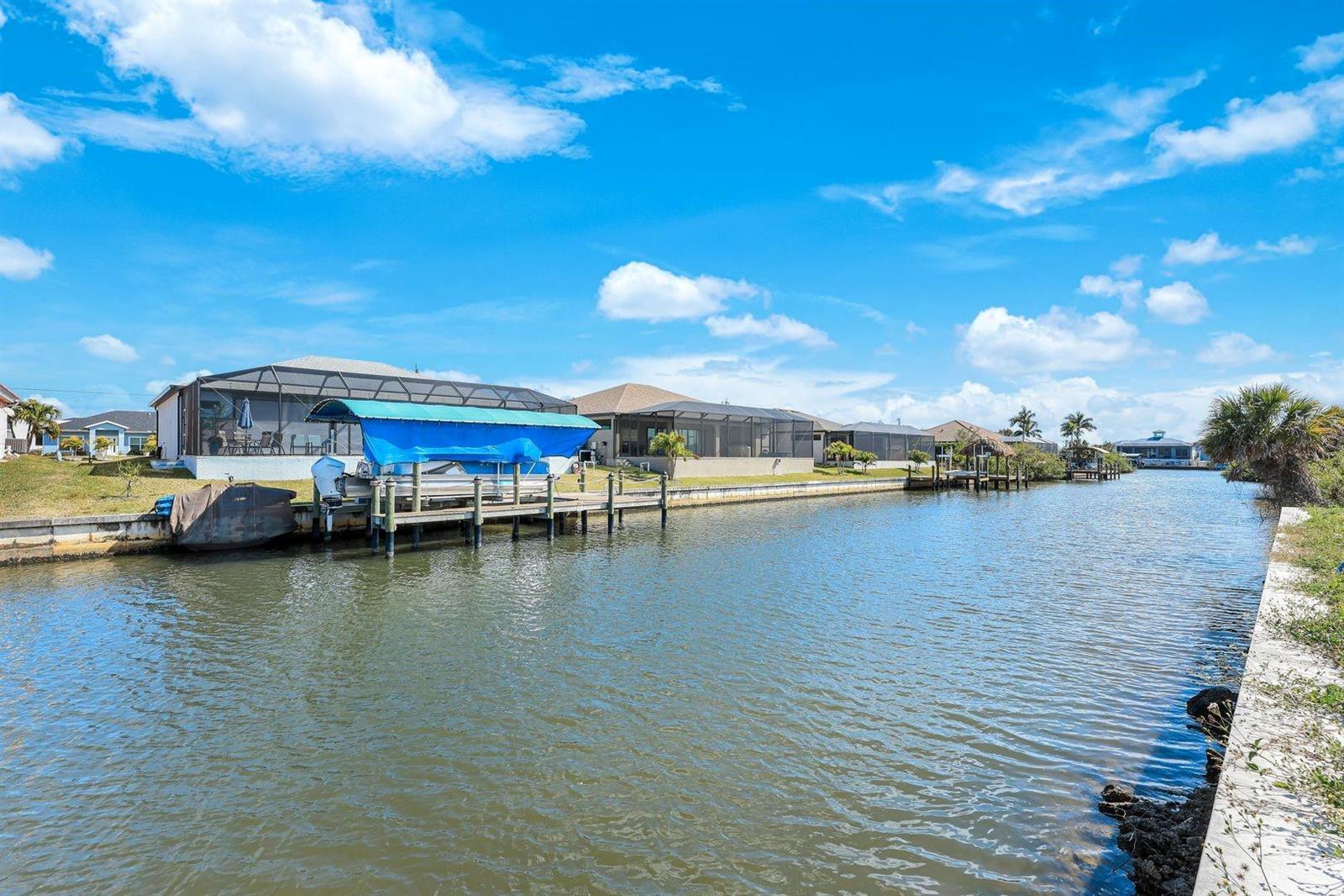 A canal view showing waterfront homes with boat docks and screened-in lanais under a blue sky — 1925 NW 34th Place, Cape Coral FL 33993, CAPE CORAL, FL