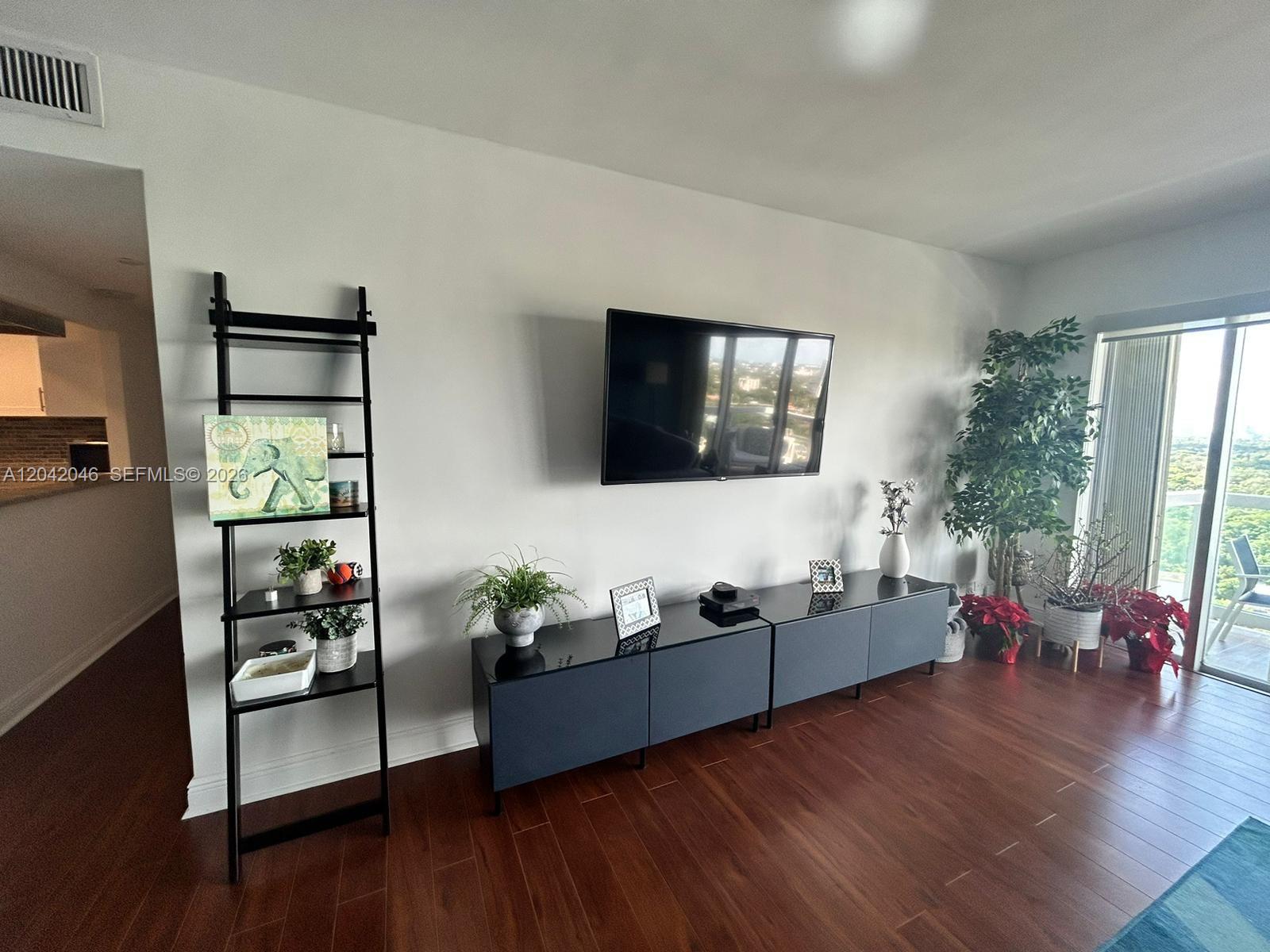 A living room features a wall-mounted television, a dark media console, and a black ladder shelf — 2451 Brickell Ave # 20M, Miami FL 33129, MIAMI, FL