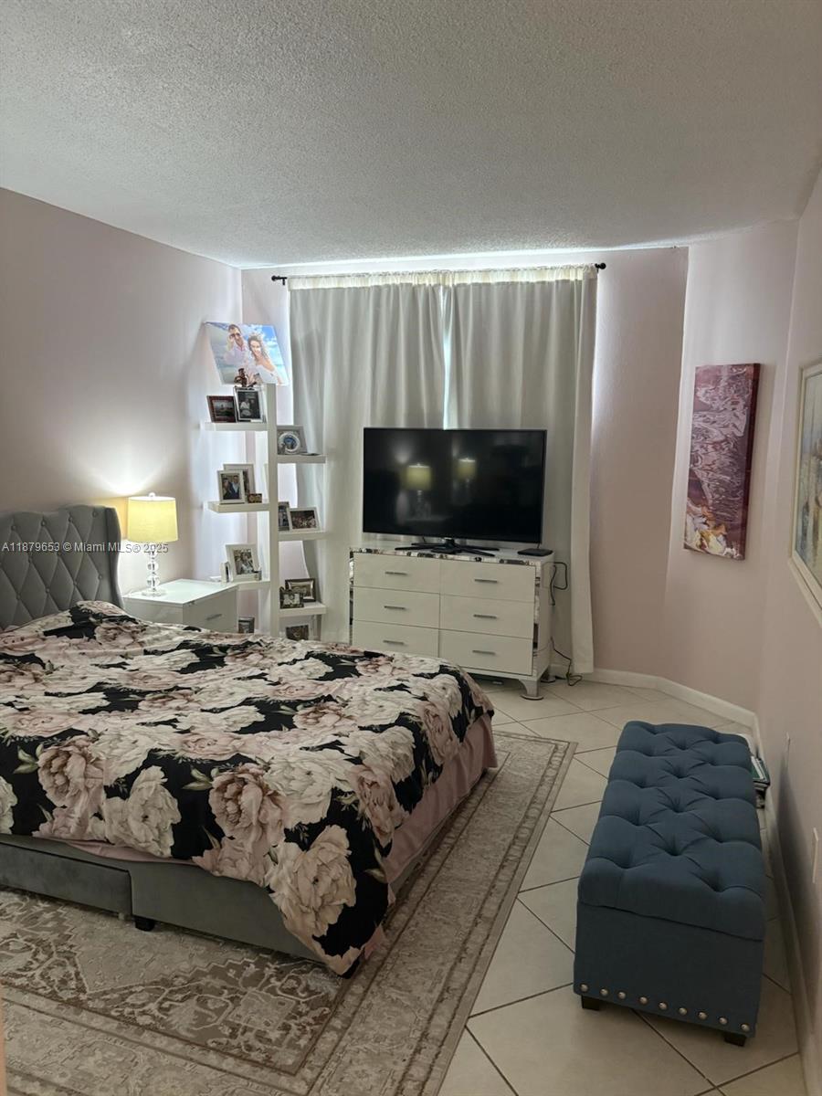 A bedroom features a tufted gray headboard, floral bedding, a white dresser, and a blue bench — 1965 S Ocean Dr # 7D, Hallandale Beach FL 33009, HALLANDALE BEACH, FL