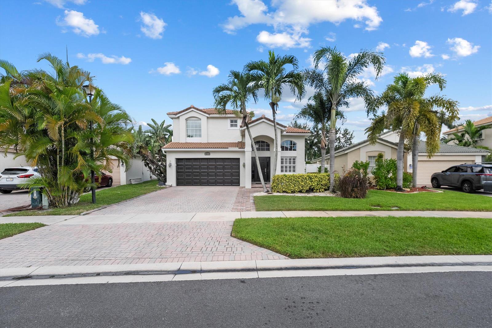 A two-story suburban house with a paved driveway, palm trees, and a dark garage door — 4033 Bluff Harbor Way, Wellington FL 33449, WELLINGTON, FL