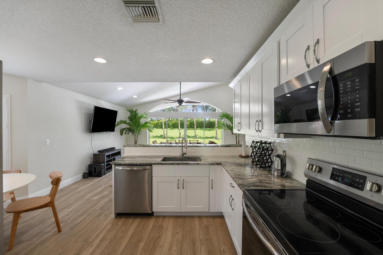 A kitchen with white cabinets, granite countertops, and stainless steel appliances overlooks a living area — 4033 Bluff Harbor Way, Wellington FL 33449, WELLINGTON, FL