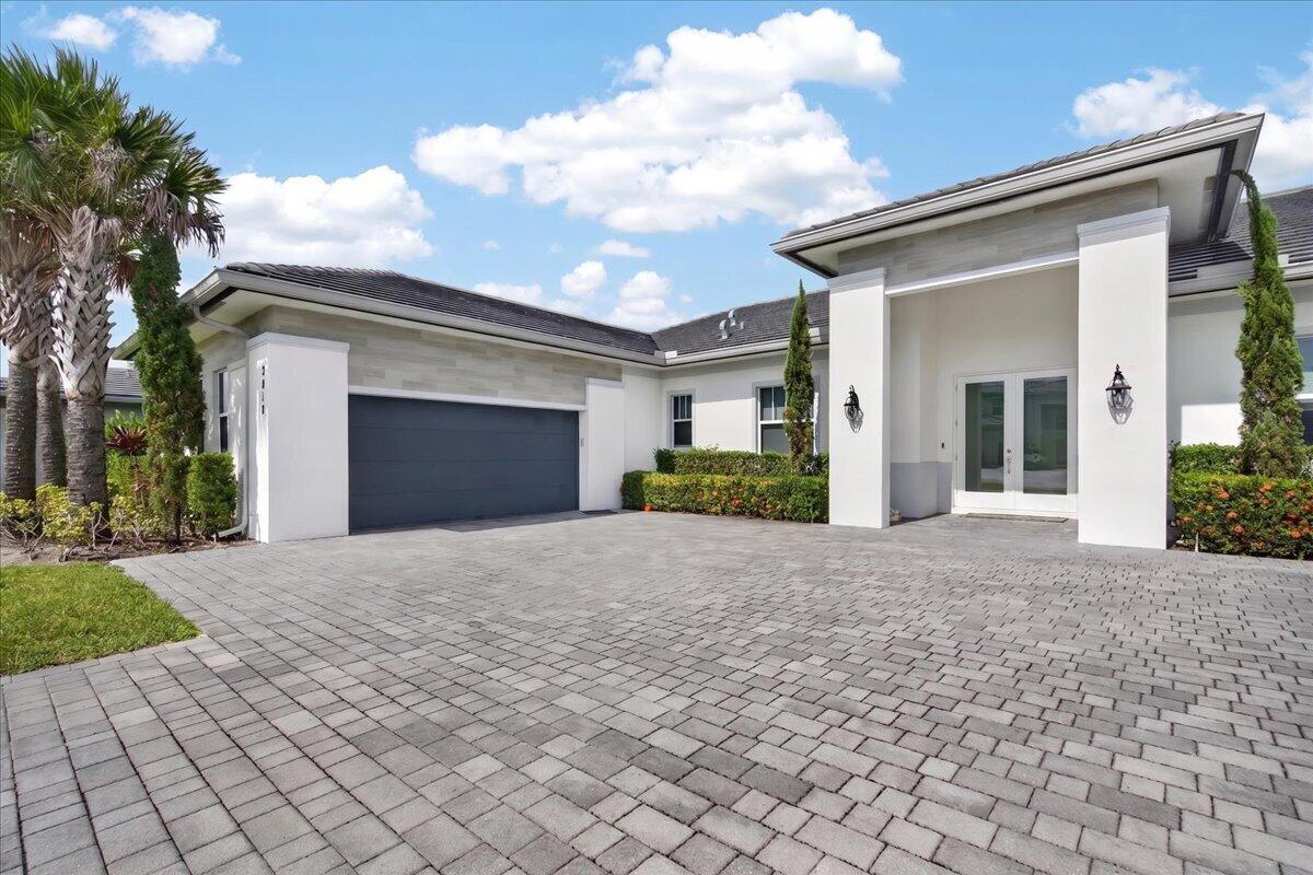 A modern single-story house features a gray garage door, white pillars, and a paved driveway — 2010 Meadows Drive, Davie FL 33324, DAVIE, FL
