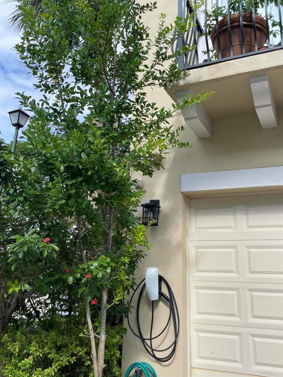 An exterior view of a house wall featuring a mounted EV charger and a tree — 552 NW 39th Circle N, Boca Raton FL 33431, BOCA RATON, FL