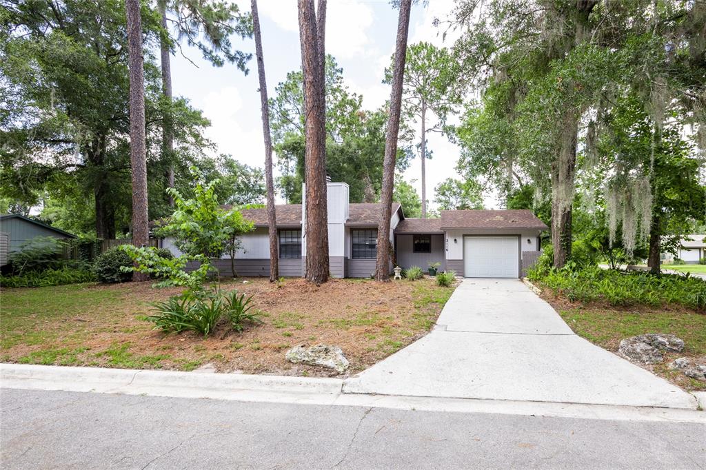 A single-story house with a white garage, gray siding, and tall pine trees in front — 2116 SW 73RD STREET, GAINESVILLE, FL