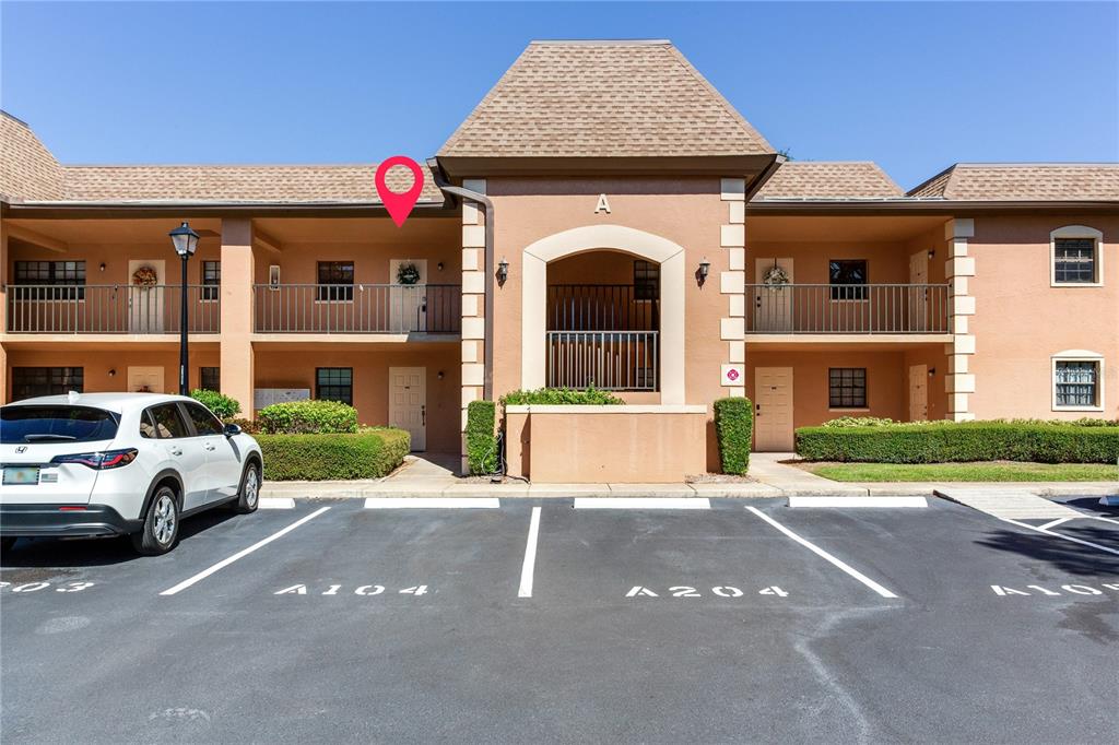 A two-story apartment building exterior features tan stucco walls, a brown shingled roof, and balconies — 12900 VONN ROAD UNIT A204, LARGO, FL