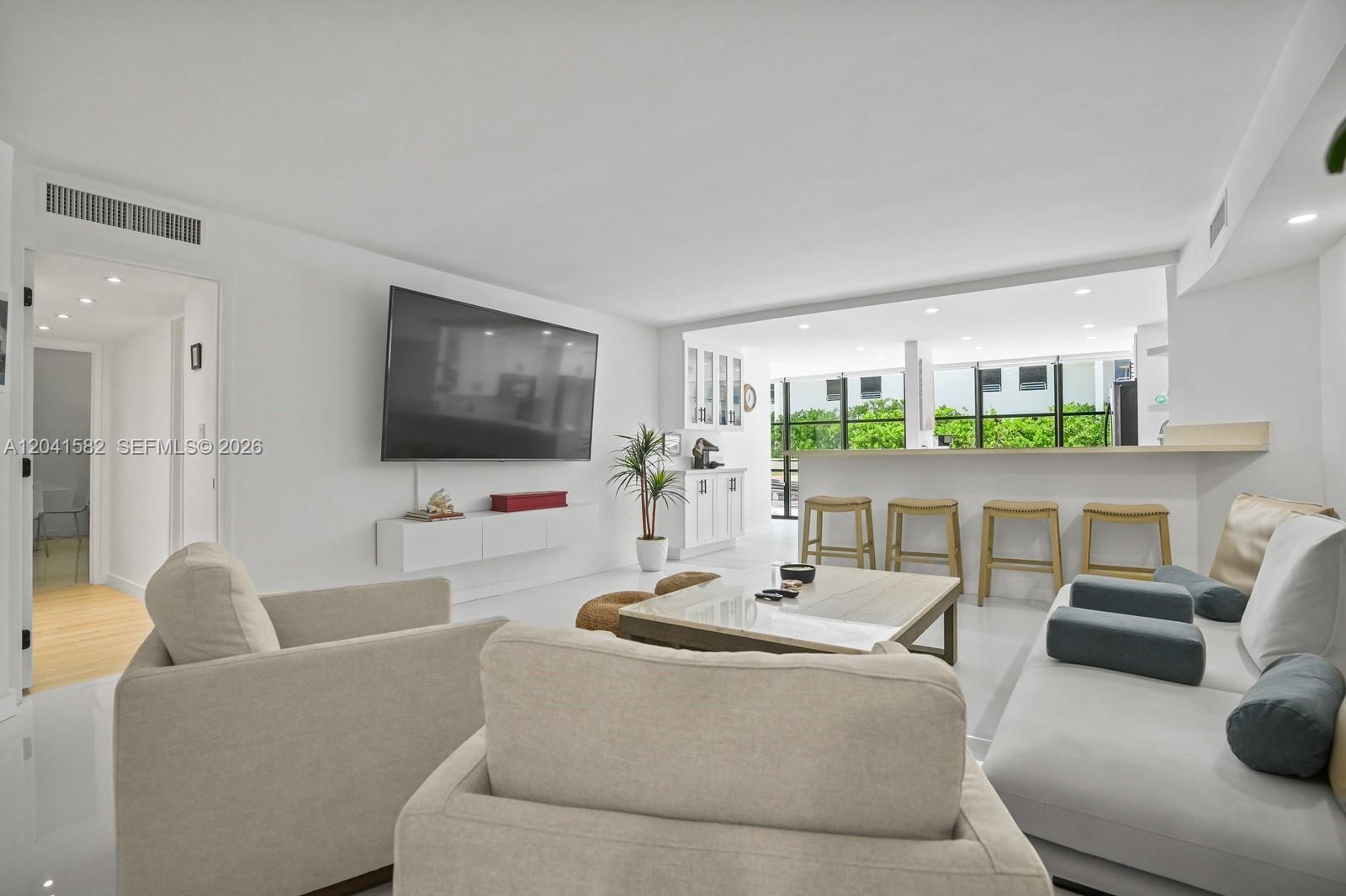 A bright, white-walled living room features a mounted television, a sofa, and a breakfast bar — 6423 Collins Ave # 203, Miami Beach FL 33141, MIAMI BEACH, FL