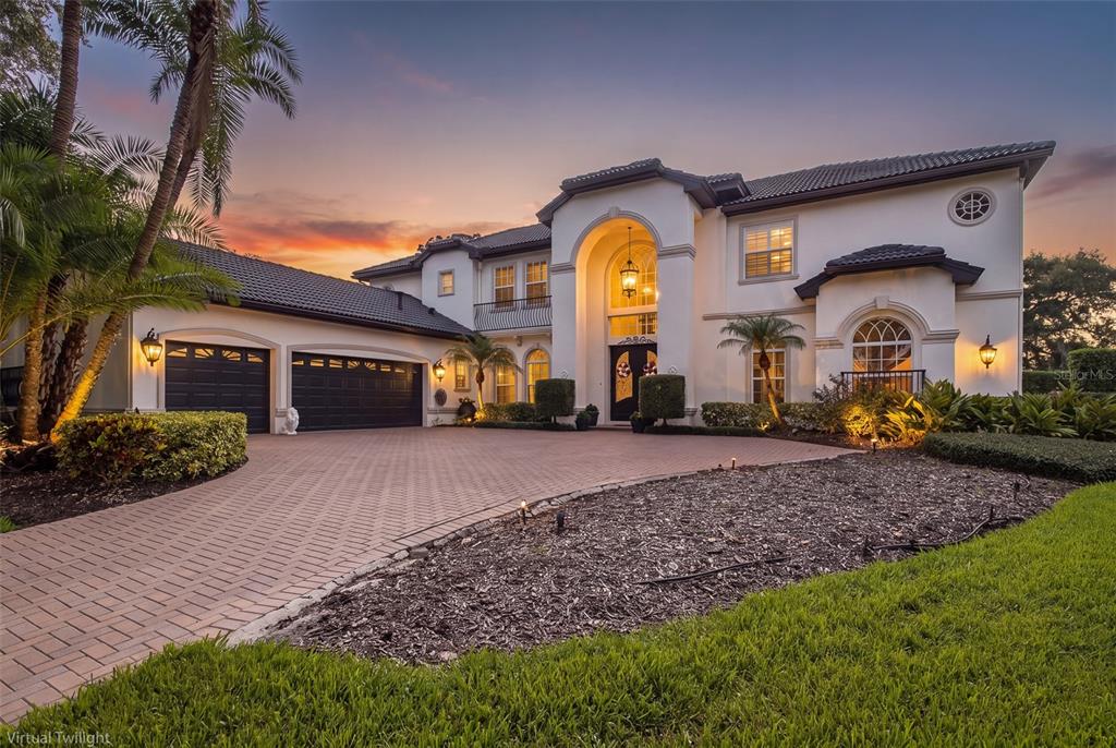 A large two-story Mediterranean-style house with a paved driveway and a three-car garage at dusk — 10628 PONTOFINO CIRCLE, TRINITY, FL