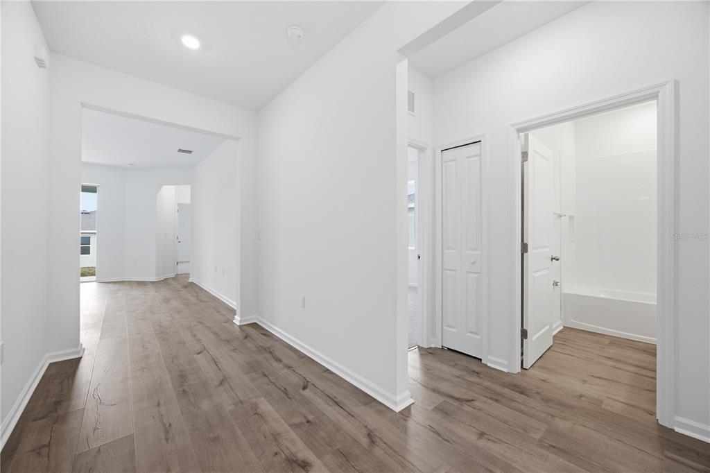 A hallway with wood-look flooring leads to an open living area and a bathroom — 6209 SANDERS GROVE CIRCLE, OKAHUMPKA, FL